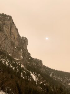 Steile Felswand im Justistal mit Schnee und Nadelwald, darüber ein milchiger Winterhimmel im Berner Oberland.