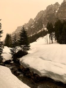 Kleiner Bach im Justistal, der sich zwischen hohen Schneewänden durchzieht, mit alpiner Winterlandschaft im Hintergrund.