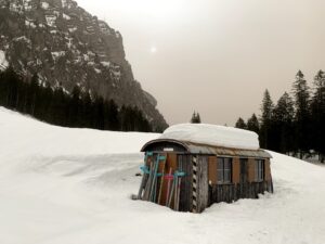 Kleine Alphütte im tief verschneiten Justistal mit Skiern an der Wand, umgeben von steilen Felswänden im Berner Oberland.