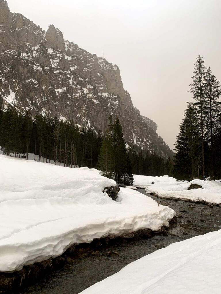 Offenes Hochtal im Justistal mit Bachlauf, verschneiten Wiesen und Bergen während einer Winterwanderung.