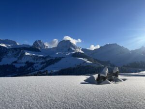 Verschneite Alpenlandschaft mit Holzbank im Schnee und weiter Aussicht auf winterliche Schweizer Berge