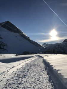 Präparierter Winterwanderweg durch tief verschneite Alpenlandschaft mit Sonne und klarer Fernsicht