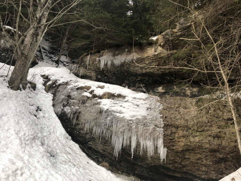 Gefrorene Felswand mit Eiszapfen entlang des Hörelirundwegs bei Adelboden im Winter