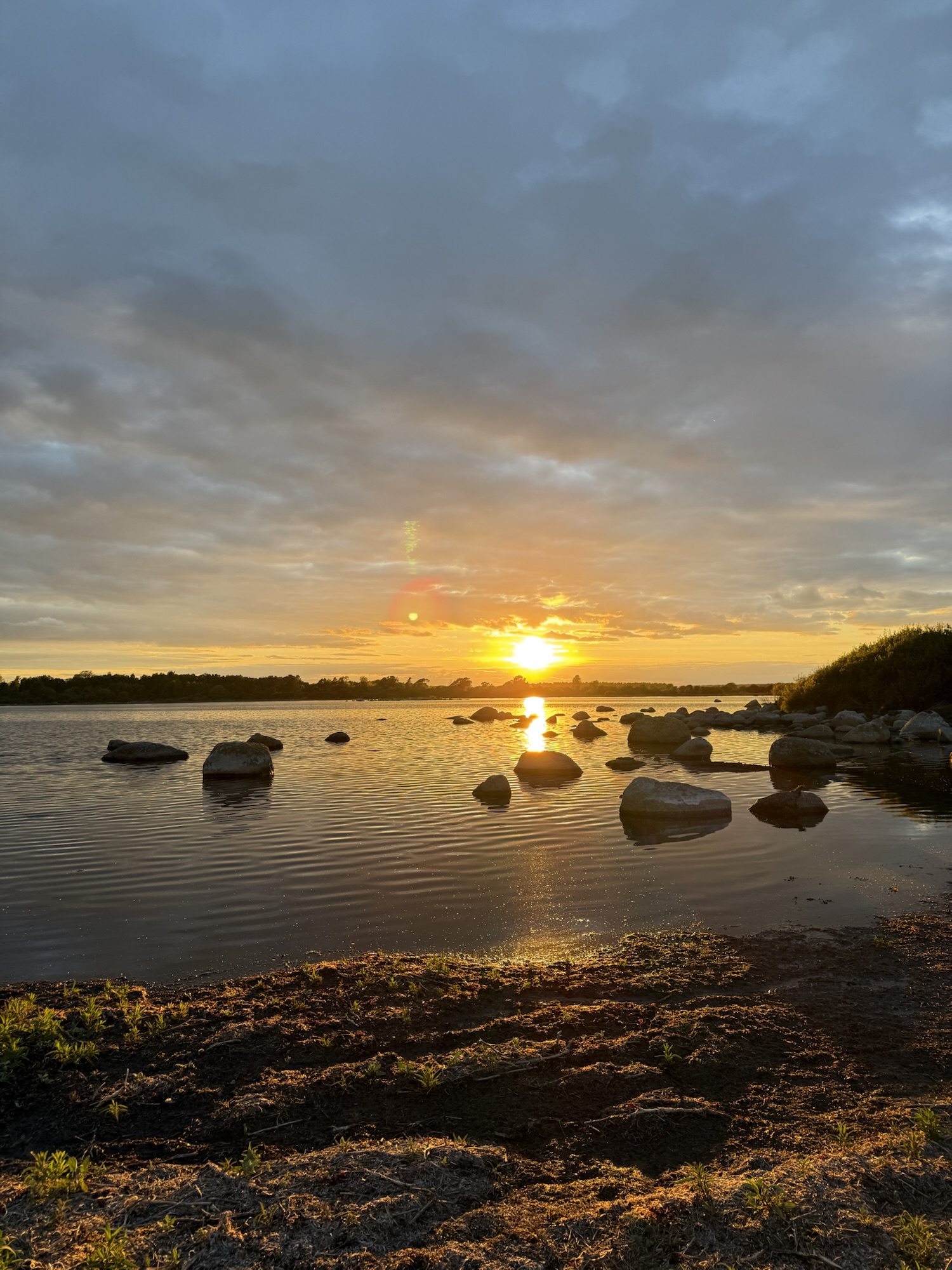 Goldener Sonnenuntergang über einem ruhigen See mit verstreuten Felsen im Wasser, warmes Licht spiegelt sich auf der Oberfläche, friedliche Abendstimmung in der Natur.