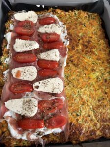 Zucchini-Karotten-Boden belegt mit Frischkäse, Rohschinken, Cherrytomaten und Mozzarella vor dem Zusammenklappen zu einem gesunden Wrap