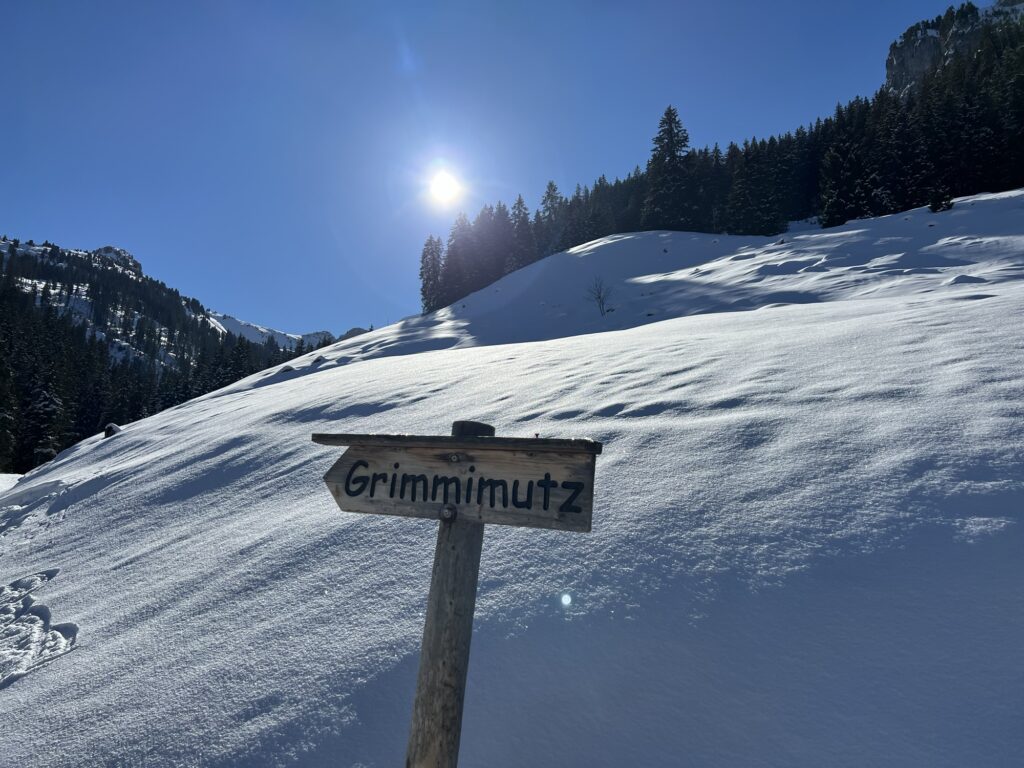 Wegweiser „Grimmimutz“ auf verschneiter Winterwanderung im Diemtigtal bei strahlendem Sonnenschein