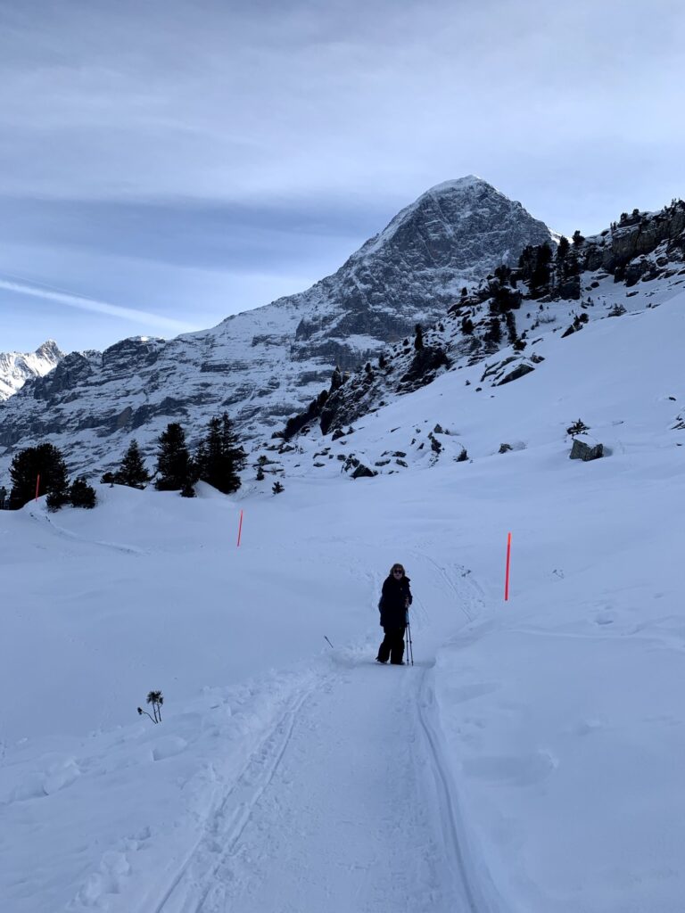 Winterwanderweg in den Schweizer Alpen mit Wanderin auf Schneeweg, umgeben von steilen Felswänden und Bergkulisse
