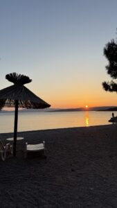 Sonnenuntergang am Strand auf der Insel Krk mit goldenem Licht, ruhigem Meer und Strohschirmen im Vordergrund.