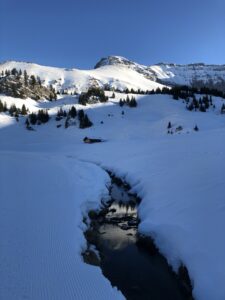 Winterwanderweg auf der Elsigenalp mit kleinem Bach zwischen verschneiten Ufern