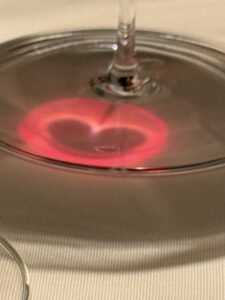 Reflexion eines roten Herzens im Boden eines Weinglases – ein leuchtendes Symbol der Liebe im Kerzenschein.