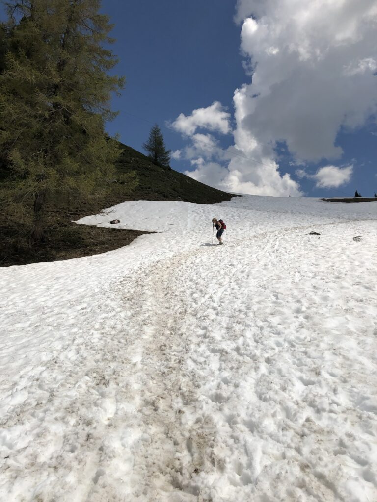 Wanderin überquert Altschneefeld beim Frühlingswandern in den Schweizer Bergen unter blauem Himmel
