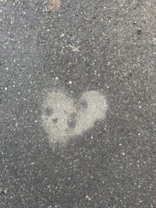 Ein herzförmiger Fleck aus trockenem Asphalt, umgeben von nasser Strasse – Liebe hebt sich selbst im Regen sichtbar hervor.