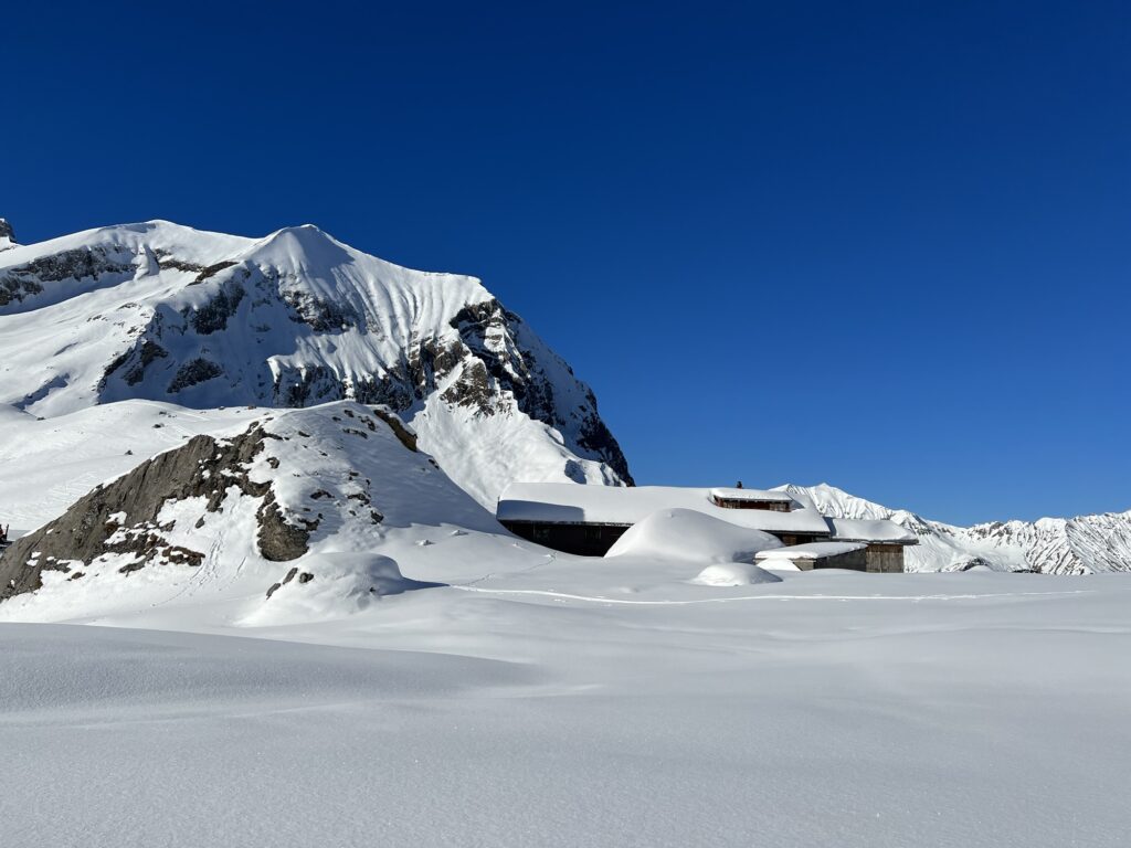 Verschneite Alphütten und Felsen auf der Engstligenalp mit Blick auf die umliegende Bergwelt