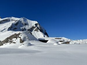 Verschneite Alphütten und Felsen auf der Engstligenalp mit Blick auf die umliegende Bergwelt