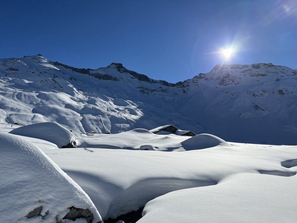 Wintersonne über der Engstligenalp mit verschneiten Hügeln, Alphütten und Bergkulisse