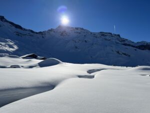 Wintersonne über der Engstligenalp mit verschneiten Hügeln, Alphütten und markanter Bergkulisse