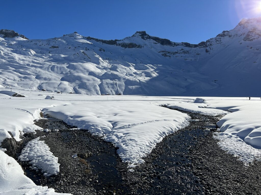 Winterlicher Bachlauf auf der Engstligenalp, umgeben von tief verschneiten Schneefeldern und steilen Bergflanken