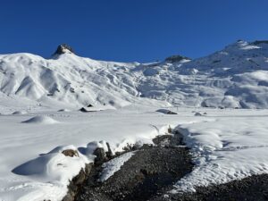 Blick über die verschneite Engstligenalp mit Bachlauf, Alphütten und weiter Berglandschaft