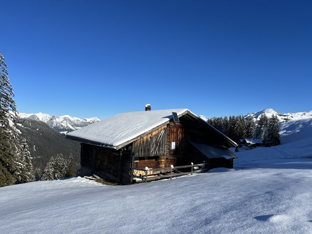 Alphütte am Rinderberg im Winter, umgeben von tiefem Schnee und sonniger Berglandschaft
