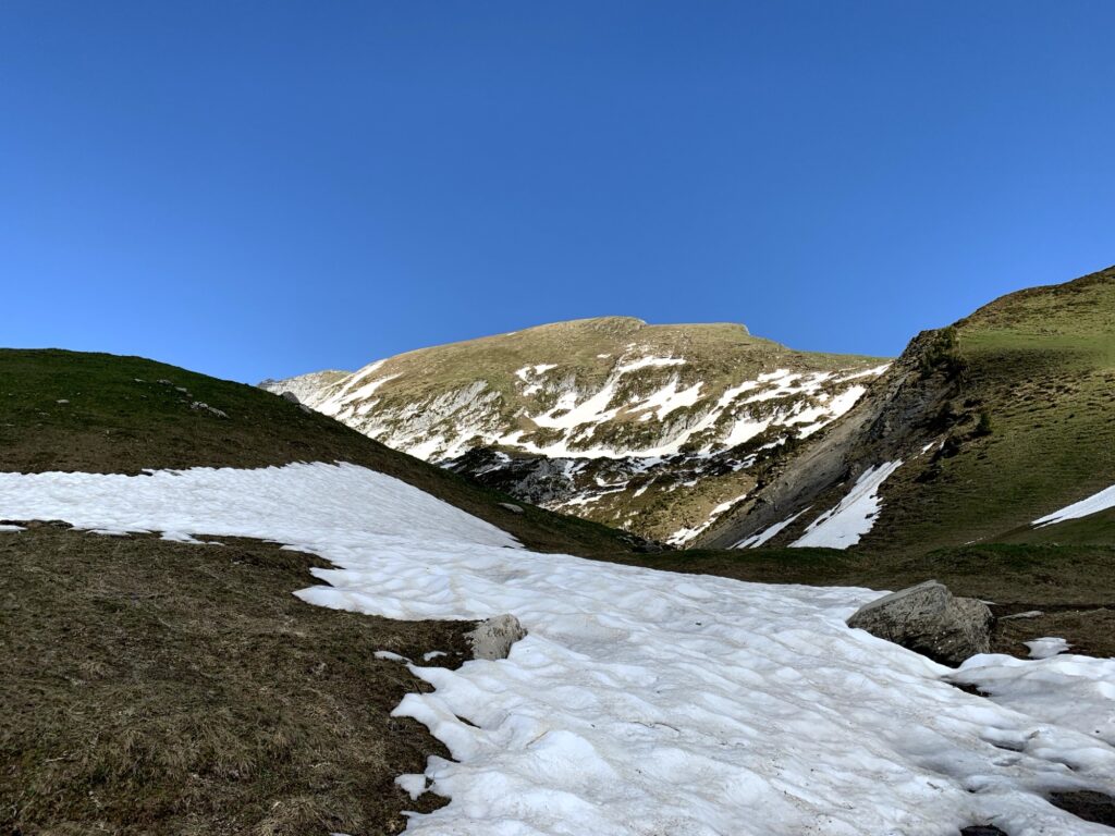 Altschneefeld auf Bergpass beim Wandern im Frühling in der Schweiz unter klarem Himmel