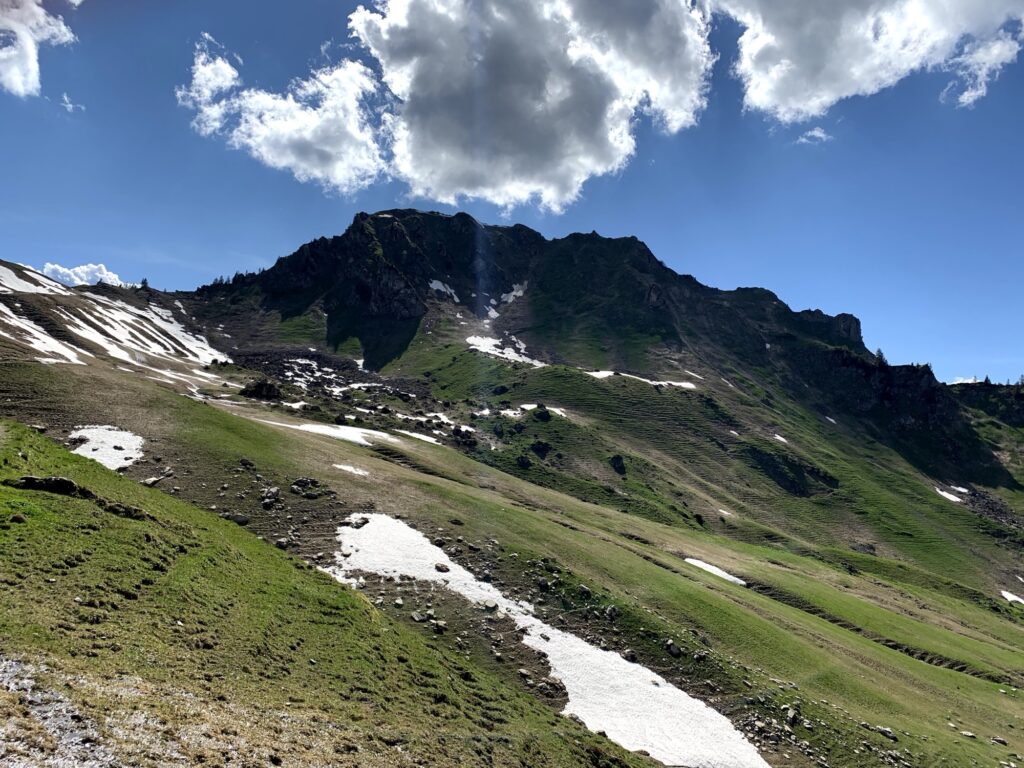 Frühlingslandschaft in den Schweizer Alpen mit Schneeresten und grünen Berghängen beim Wandern im Frühling