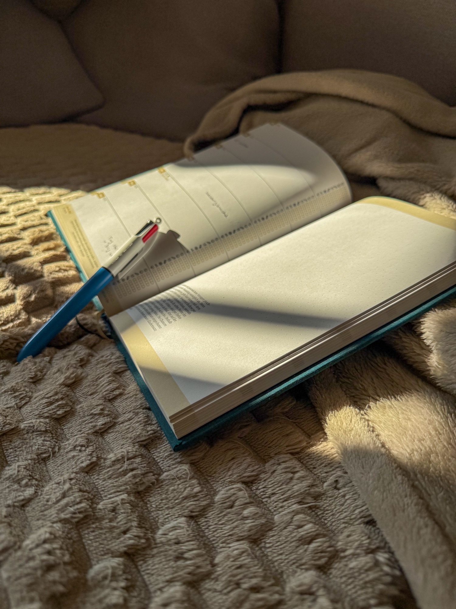 Offenes Notizbuch mit Stift auf einer kuscheligen Decke im warmen Sonnenlicht – ruhige Szene für Planung und Routinen im Alltag