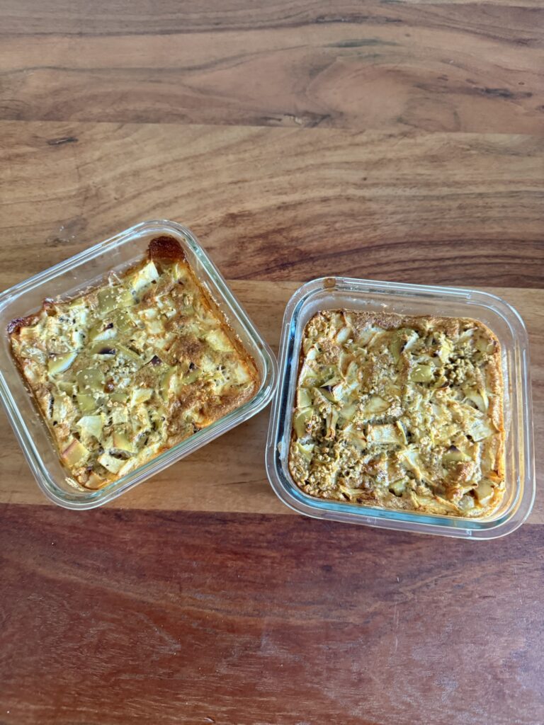 Zwei Portionen Protein Baked Oats mit Apfel in kleinen Glasformen auf Holztisch, einfaches und gesundes Frühstück zum Vorbereiten