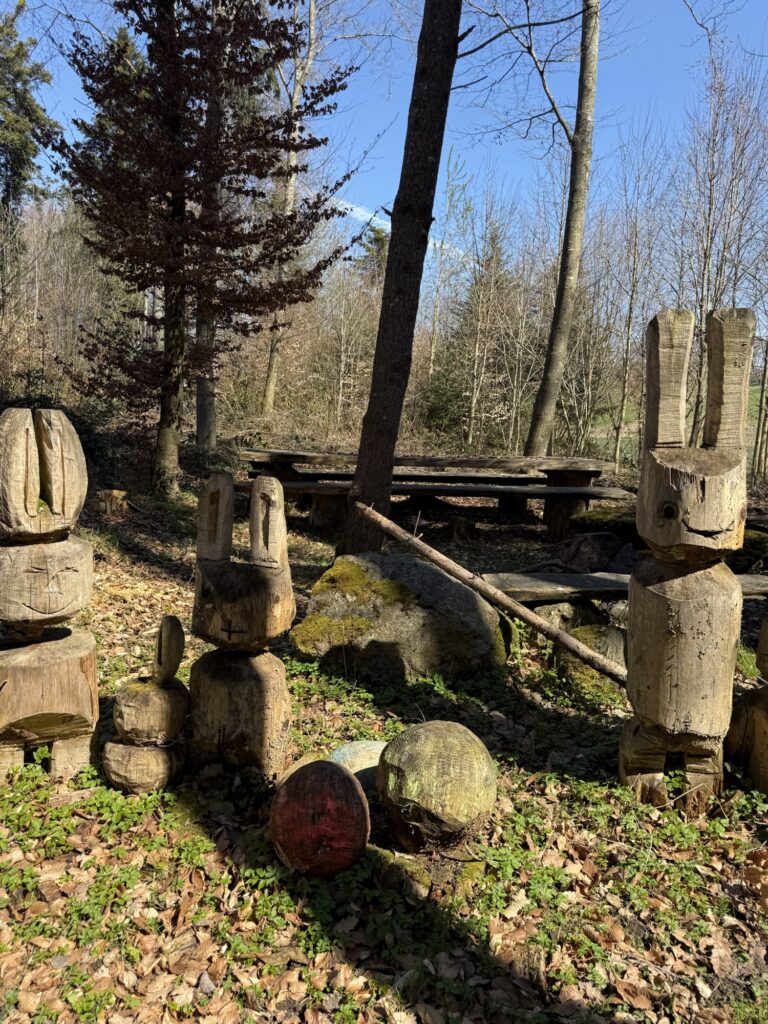 Holzfiguren im Wald am Belpberg mit Rastplatz und Frühlingssonne bei Bern