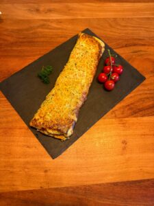 Herzhafte goldene Gemüse-Rolle auf schwarzer Schieferplatte serviert, angeschnitten mit sichtbarer Füllung. Dekoriert mit Petersilie und Cherrytomaten auf rustikalem Holztisch.