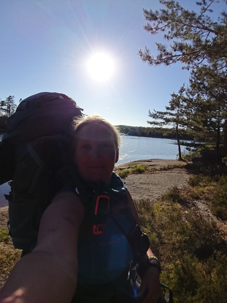 Frau alleine mit grossem Trekkingrucksack an einem See während einer Wanderung