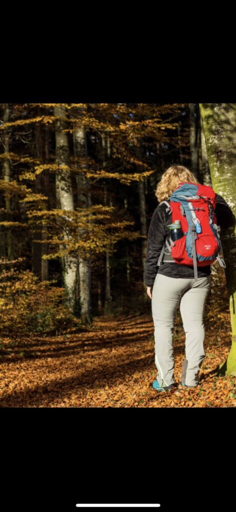 Alleine wandernde Frau mit rotem Rucksack auf einem Waldweg im Herbst